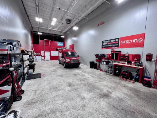 Interior of Vibrant Mobile Detail shop featuring large GTechniq Crystal Serum Ultra Accredited Installer banners on the wall, a red Ford Transit van, organized red workbenches with professional detailing tools, and metal shelving with supplies.