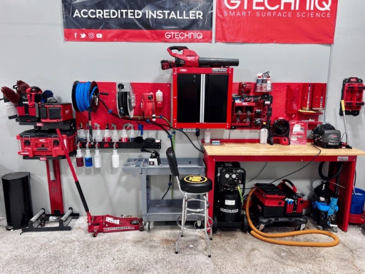 Professional detailing tool wall at Vibrant Mobile Detail featuring GTechniq Accredited Installer and Smart Surface Science banners overhead, a red pegboard wall-mounted tool organizer with polishing machines and hose reels, Milwaukee power tools, a Craftsman cabinet, NorthStar pressure washer, and a butcher block workbench.