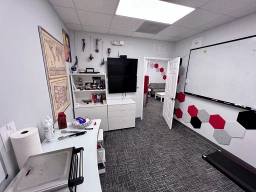 Vibrant Mobile Detail team room and founder office featuring a wall-mounted TV, large whiteboard, vintage world map, decorative hexagon panels in red gray and black, bookshelf, filing cabinet, and doorway leading to the customer lounge.