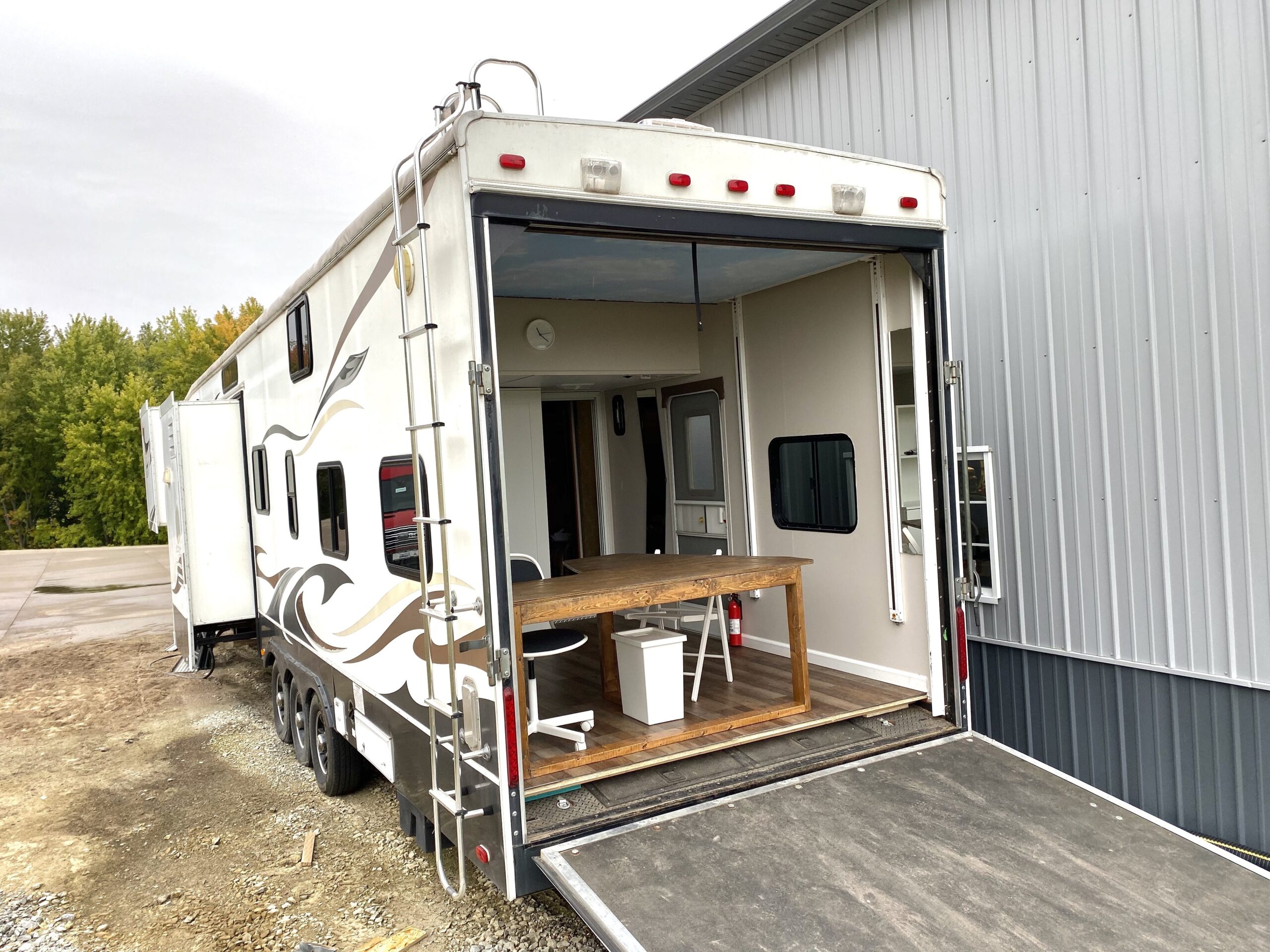 Exterior view of a large RV trailer with the back ramp open, revealing a mobile office setup.